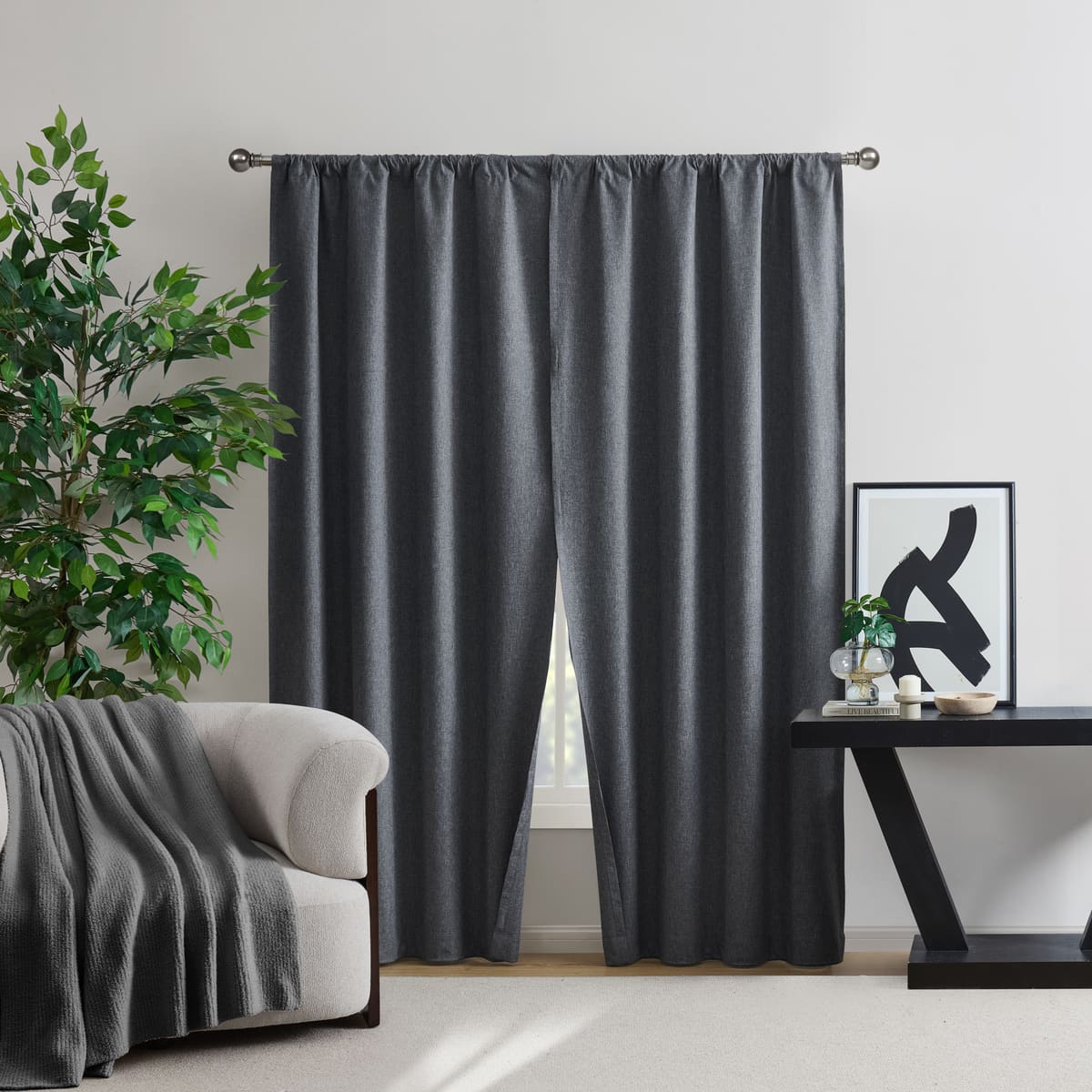 A Beekman Magnet Closure blackout pair in a charcoal tone on a rod at a window, a cream armchair with a grey throw on one side and a black console table on the other